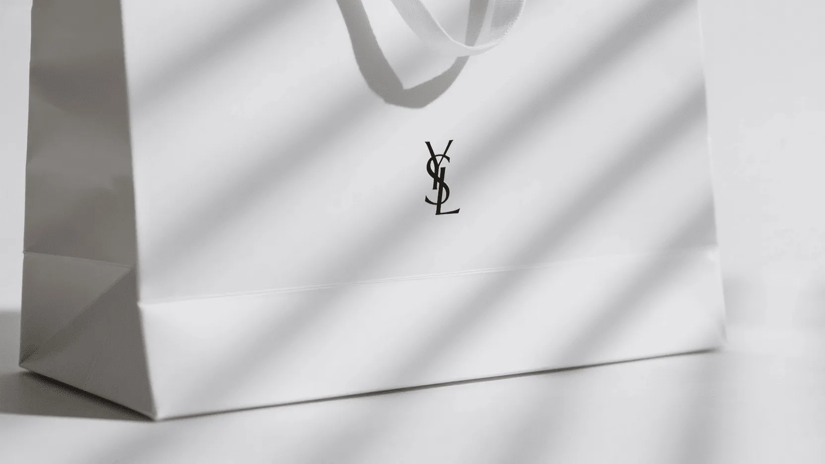 A sleek white cardboard paper bag with crisp folds and a luxury brand logo
