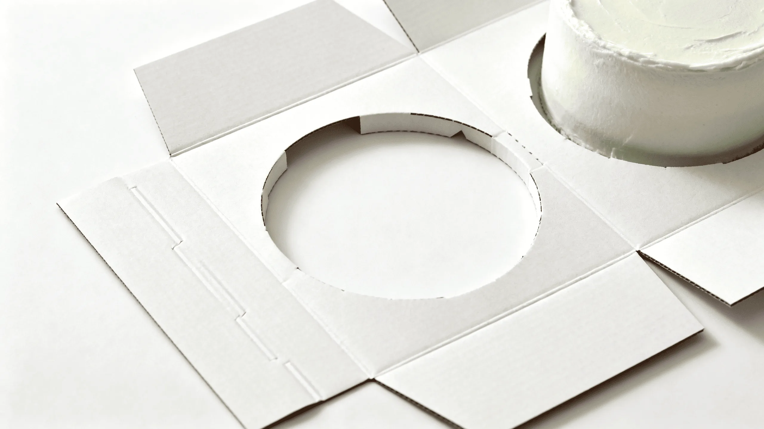 A close-up of a precision die-cut paperboard insert designed to hold a small cake securely in the center of a box.