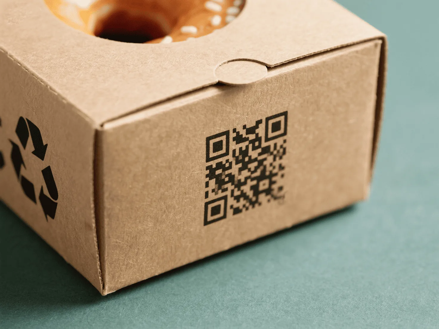 A close-up of a QR code printed on the side of a recyclable kraft paper donut box.