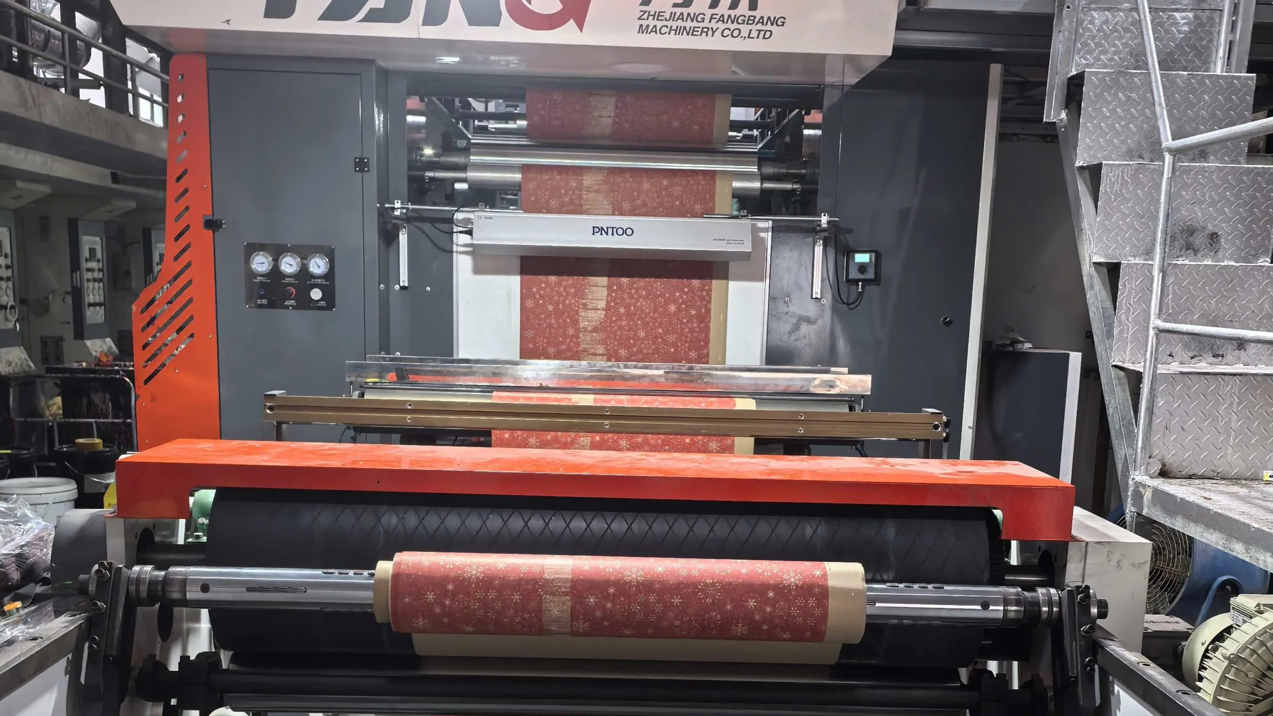 A printing press applying a simple, one-color design onto a large roll of brown kraft paper.