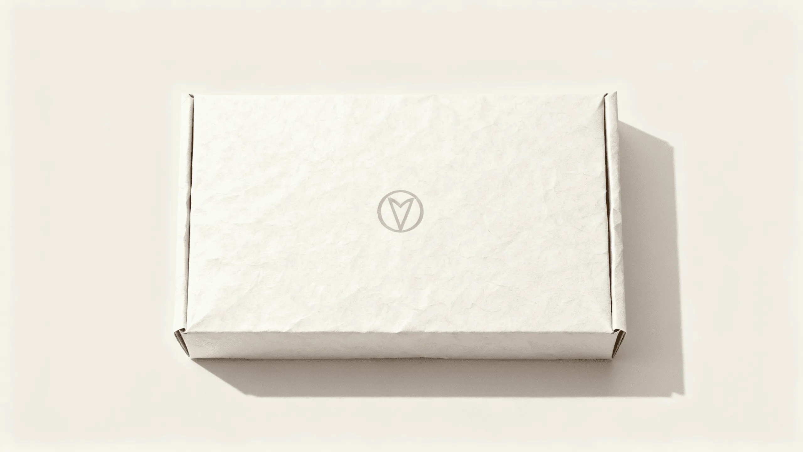 A simple, perfectly folded cosmetic box made from thick, textured off-white paper with a clean, centered logo.