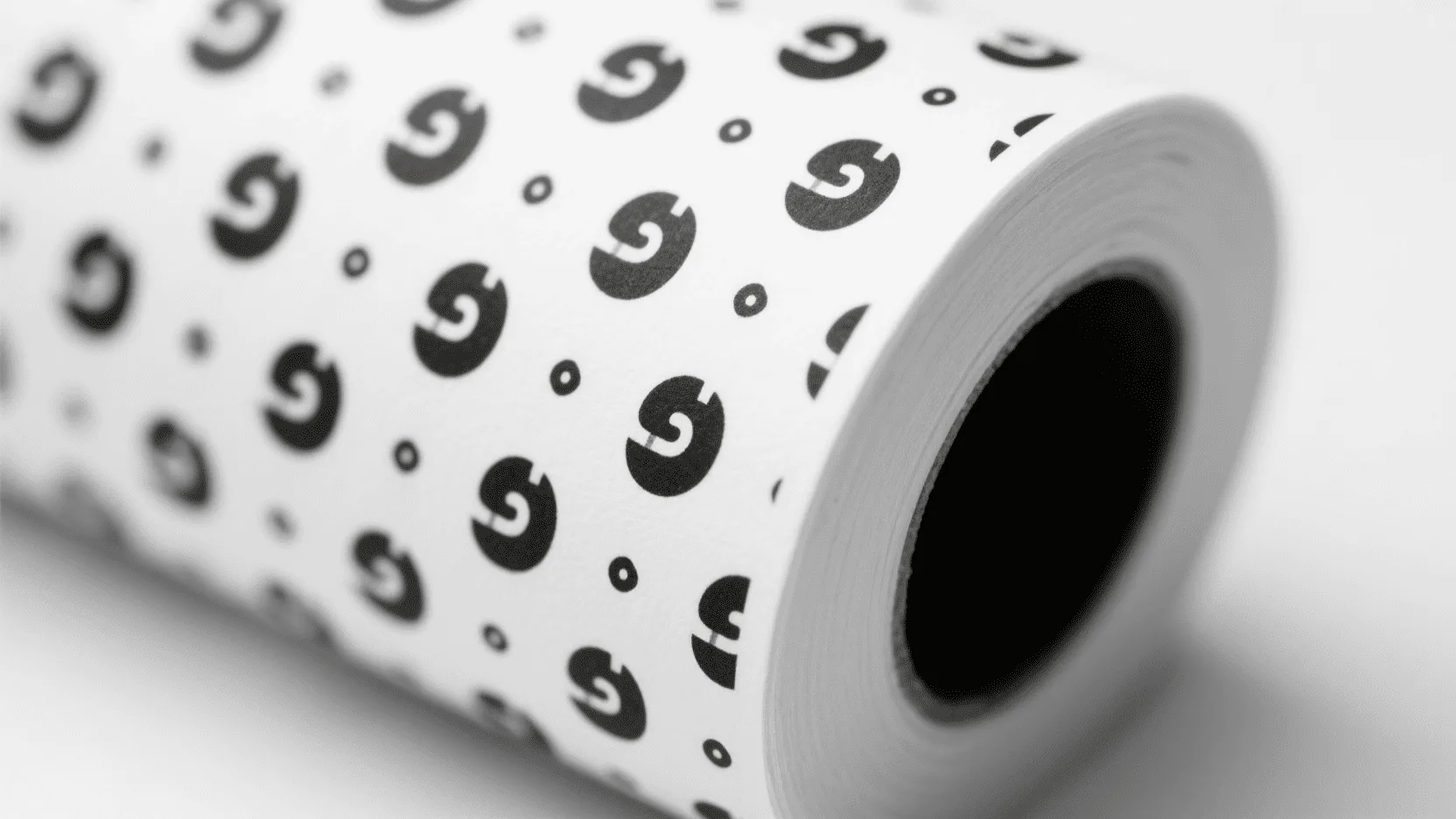 Close-up of a roll of white paper with a subtle, repeating black logo pattern.