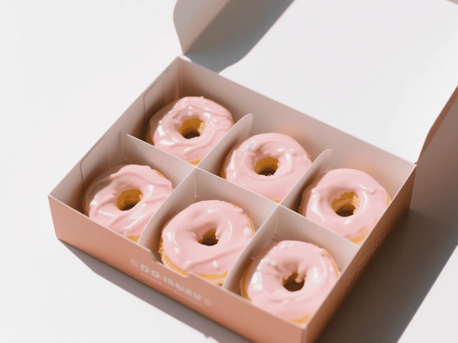 An open donut box with custom paper inserts perfectly holding each donut in place, preserving the delicate frosting.