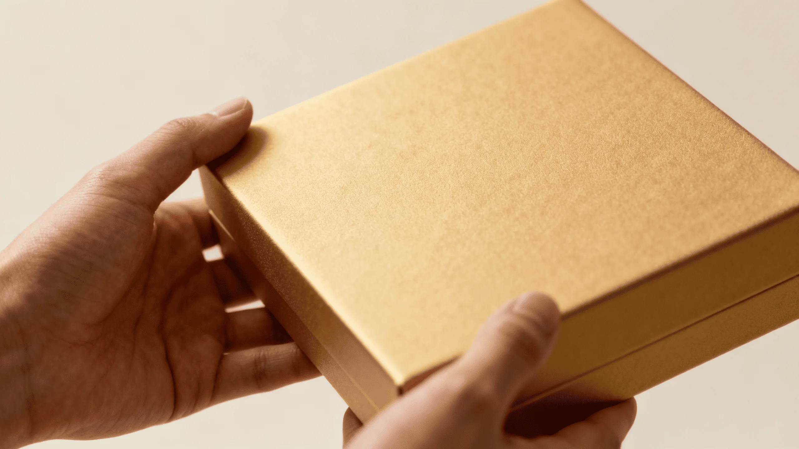 A person's hand gently holding a product box with a smooth, matte, soft-touch finish.