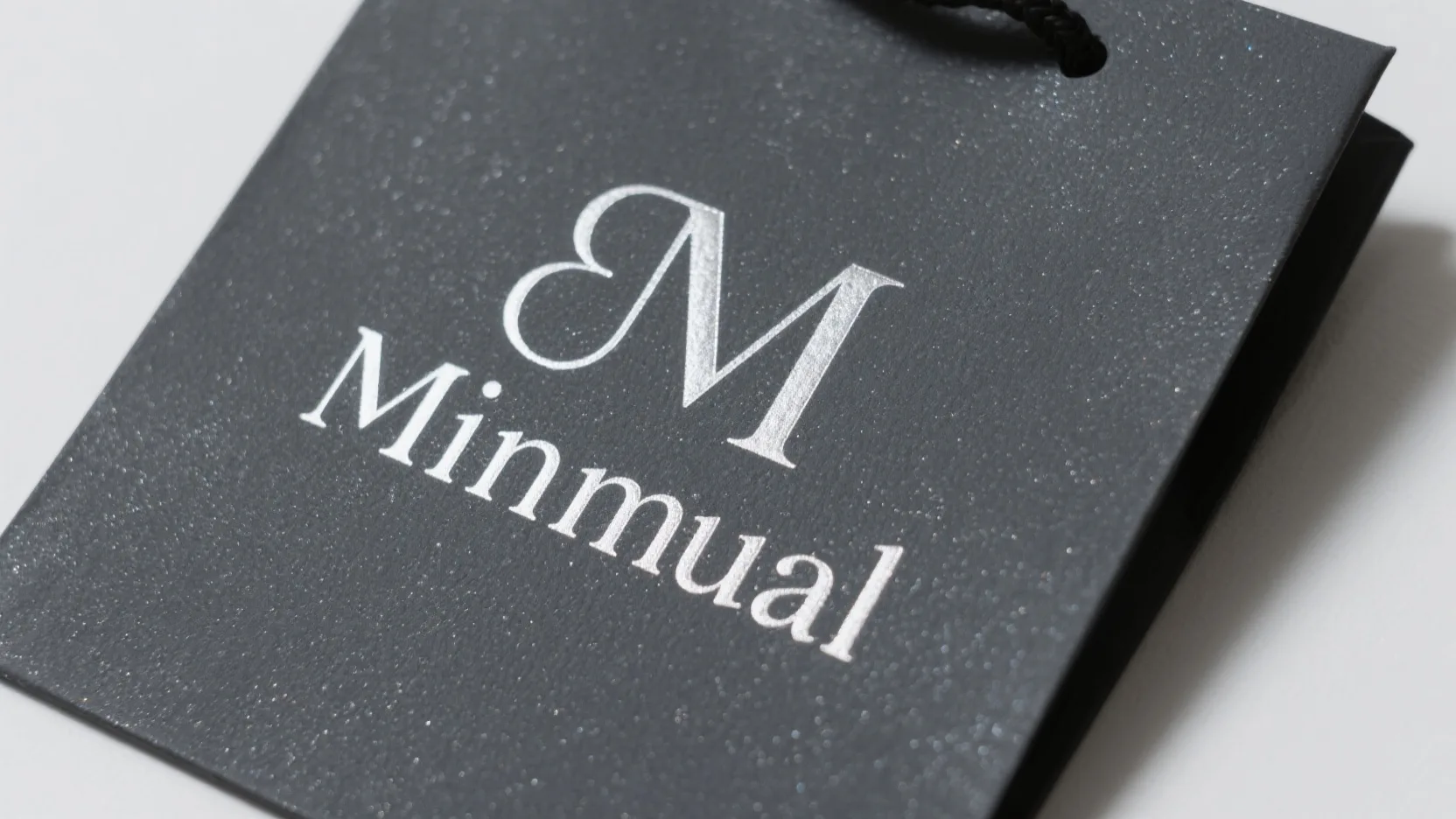 An elegant, minimalist logo hot-stamped in matte white foil on a charcoal-colored glitter paper bag, showcasing a sophisticated contrast.