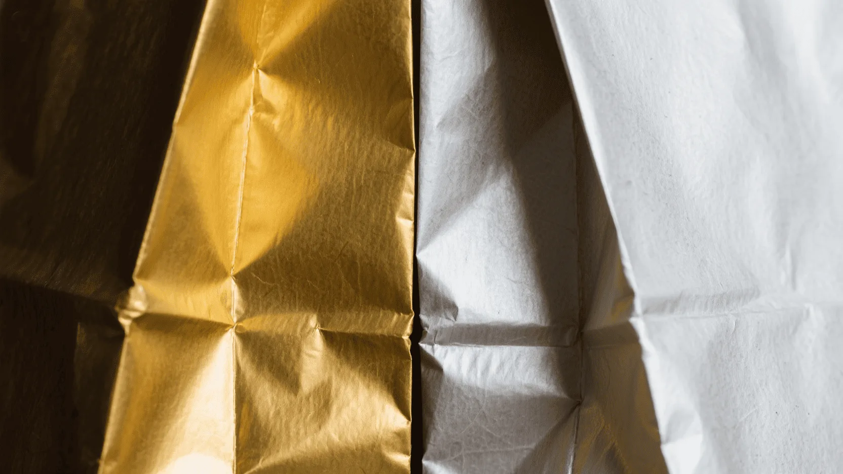 Close-up shot showing the texture of both a gold and a silver cardboard paper bag side by side.