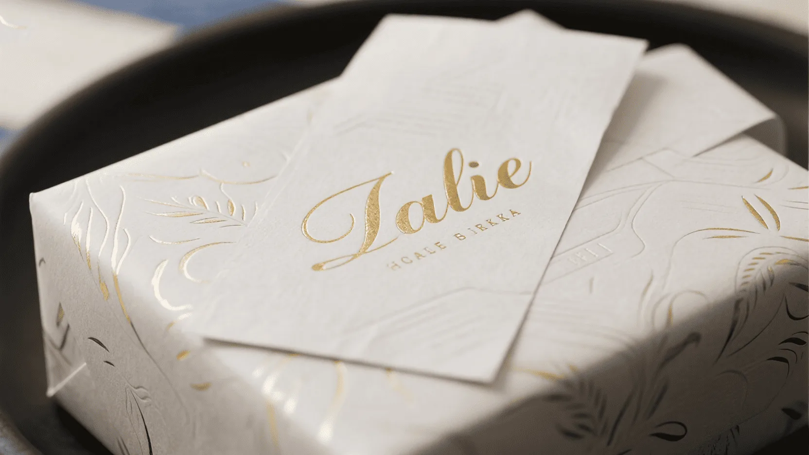 A close-up shot of white kraft wrapping paper featuring a logo with elegant gold foil stamping and a subtle embossed texture.