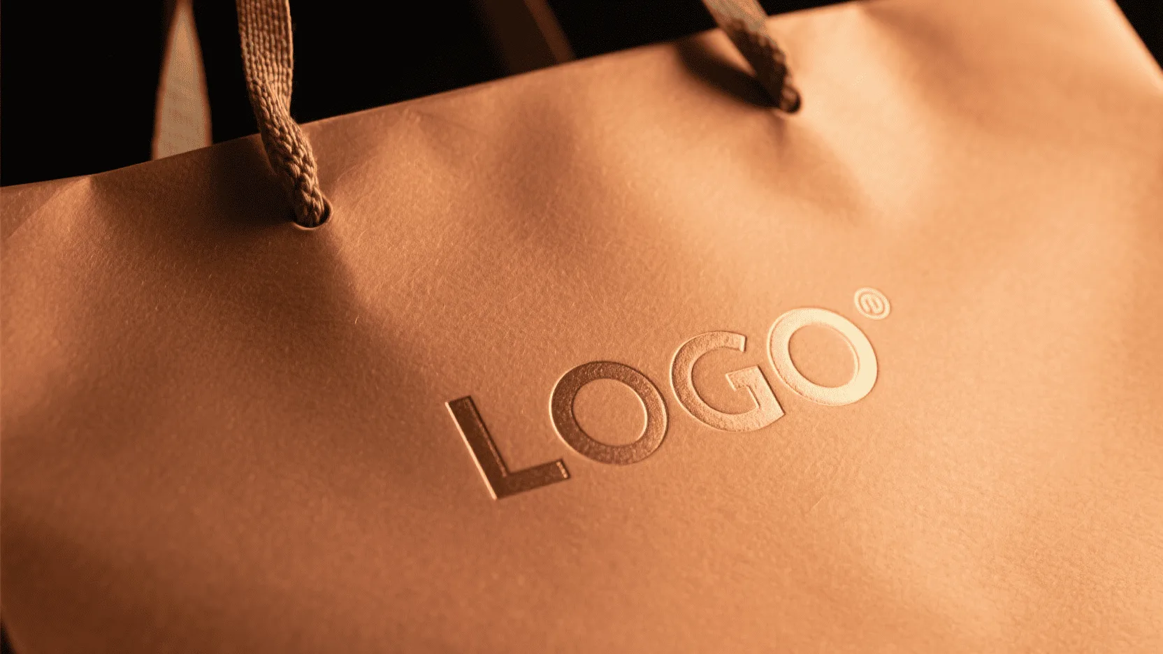 A close-up shot of shimmering gold foil being stamped onto a matte black paper bag.