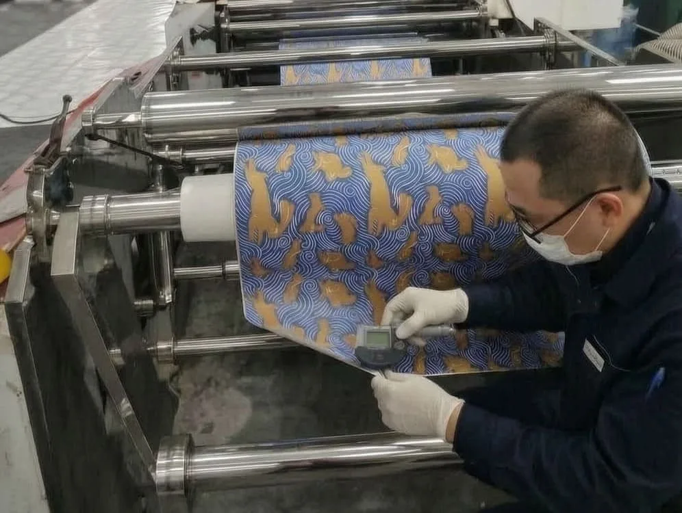 An image of a QC inspector in a factory using a digital micrometer and a gram scale to test a sample of wrapping paper, with a checklist in the background.